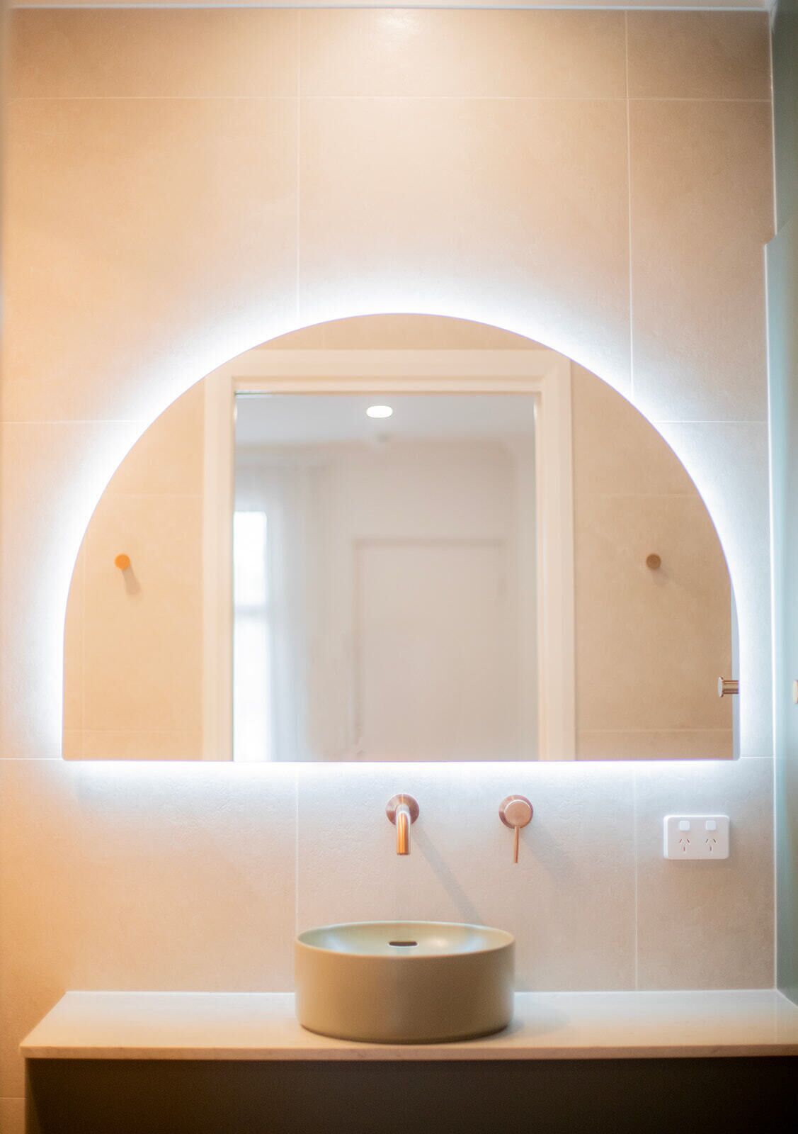 Un baño con un espejo redondo, un lavabo y una lámpara sobre él.