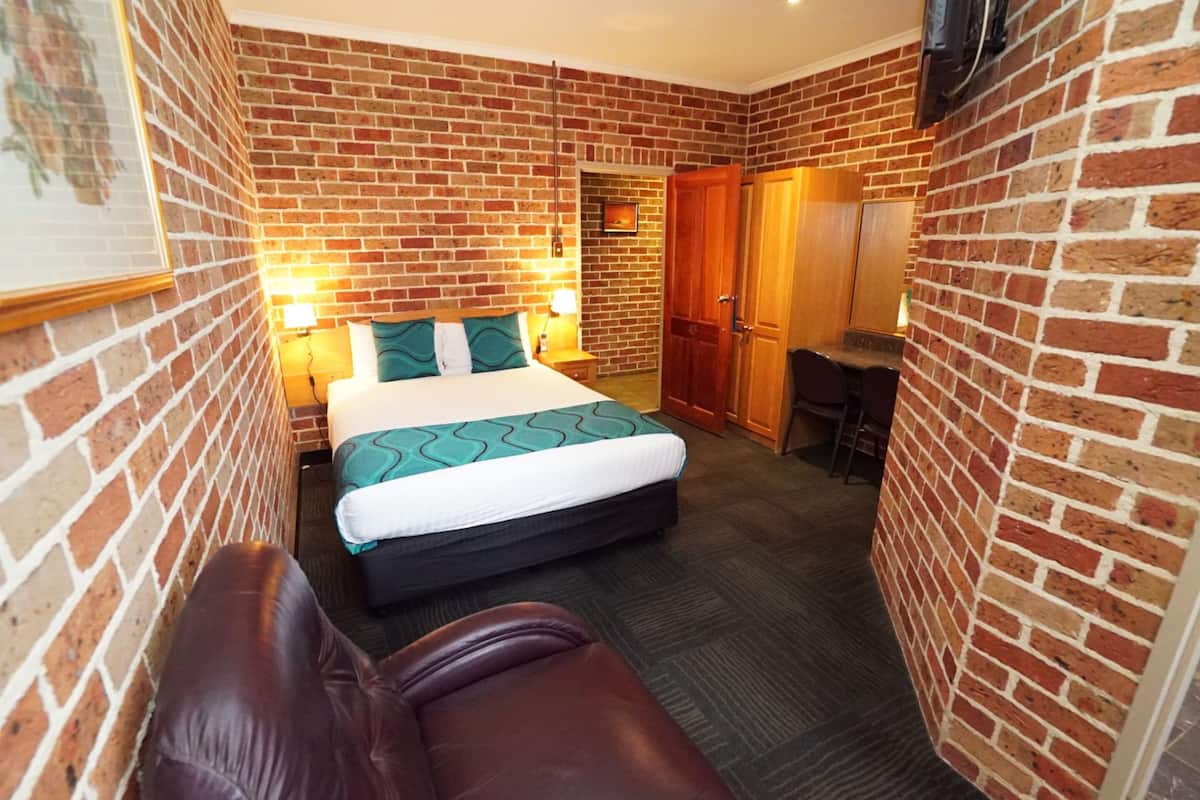 A hotel room with a brick wall, a bed with a green and white bedspread, a leather sofa, a desk, and a wardrobe.