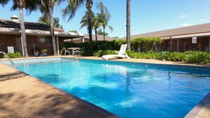 Une piscine avec des chaises longues, des palmiers et un bâtiment en briques en arrière-plan.