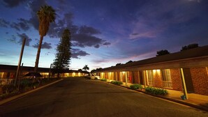 Un motel avec une rangée de chambres, un parking et un palmier.