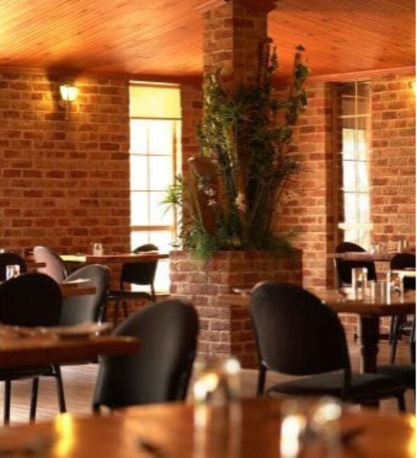 Interior de restaurante con paredes de ladrillo, techo de madera y mesas con sillas.