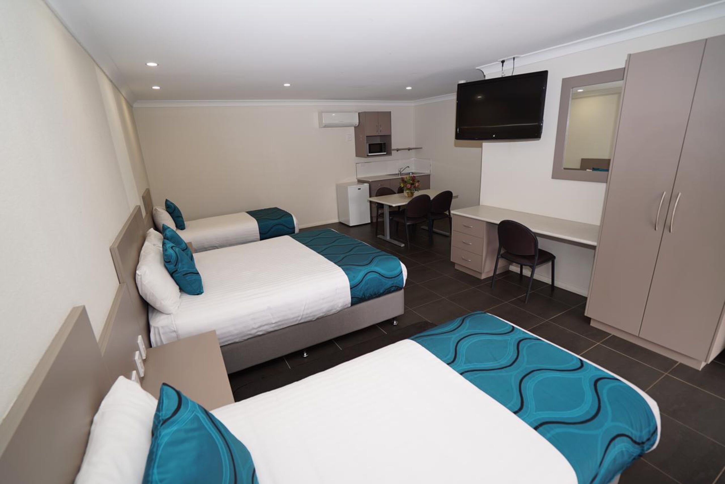 A hotel room with two beds, a desk, a chair, a TV, and a wardrobe.