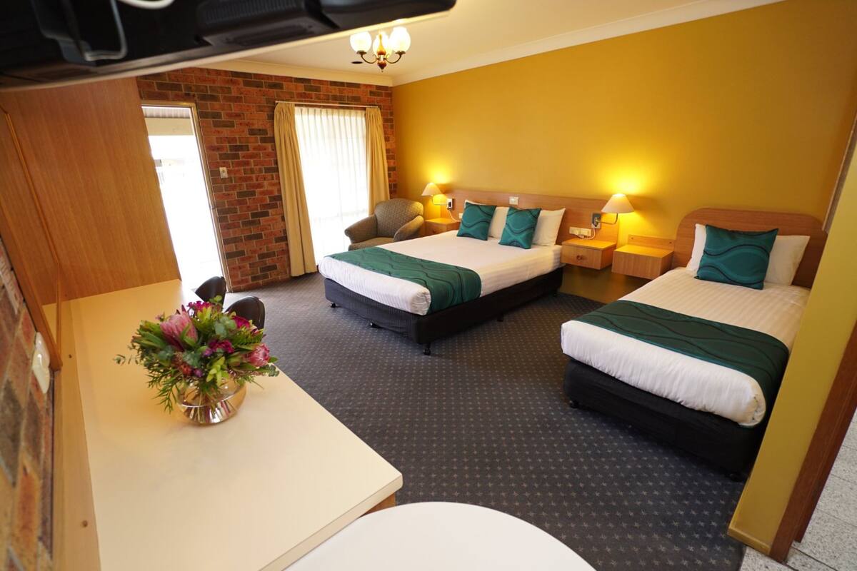 A hotel room with two beds, a desk, a chair, and a small table with a vase of flowers.