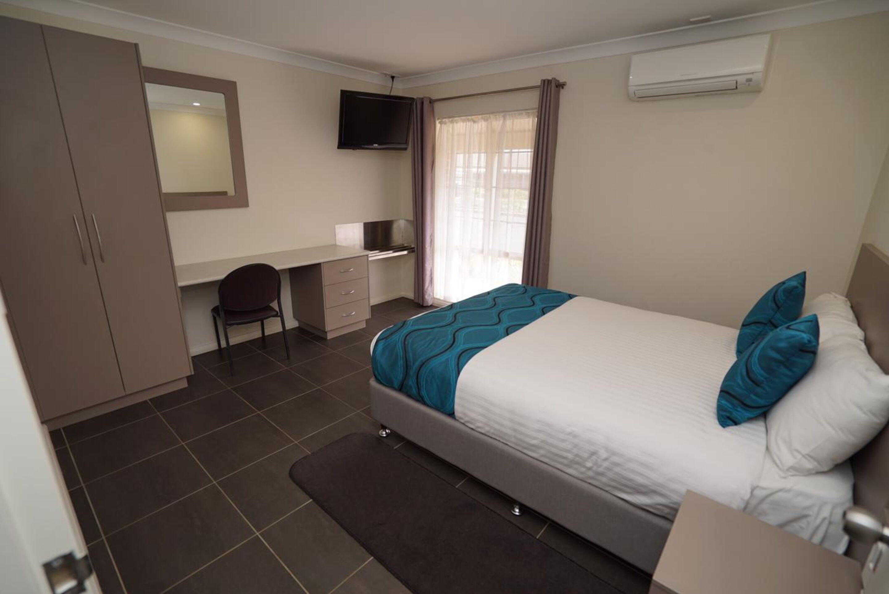 Een slaapkamer met een bed, een bureau, een stoel, een televisie en een airconditioning.