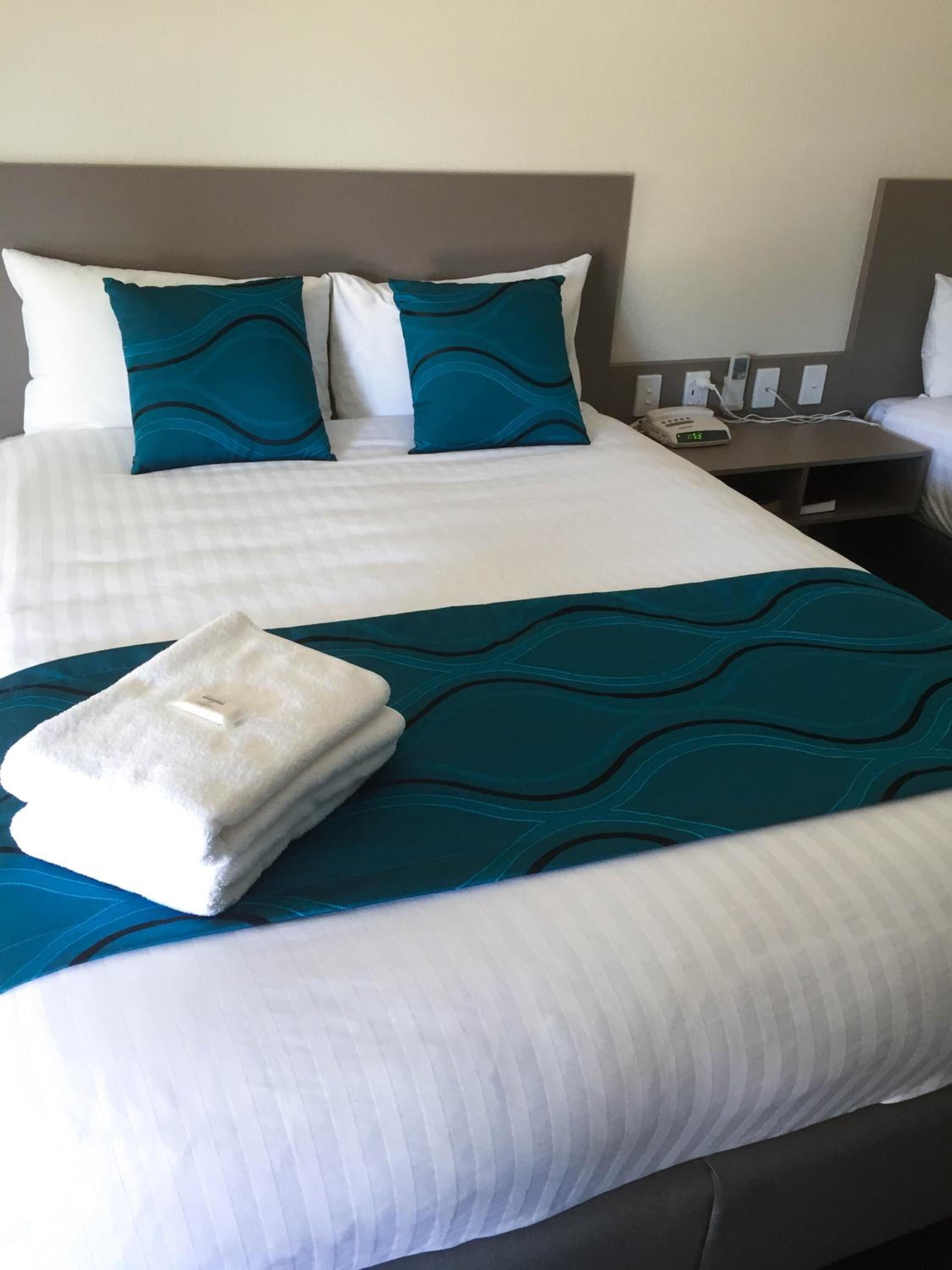 A neatly made bed with white and teal bedding, a folded white towel, and a teal throw blanket.