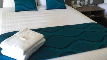 A neatly made bed with white and teal bedding, a folded white towel, and a teal throw blanket.