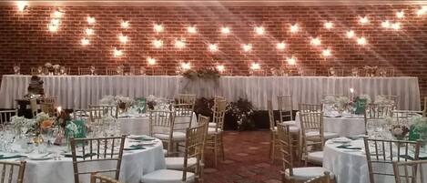 Un salón de banquetes con mesas redondas dispuestas para un evento formal, con manteles blancos y centros de mesa florales.