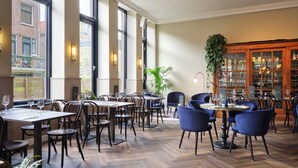 Un restaurante con techos altos, amplios ventanales y un suelo de madera con dibujo de espiga. Mesas y sillas dispuestas para comer.