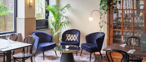 A cozy dining area with round tables, dark blue chairs, a central coffee table, and a large potted plant.
