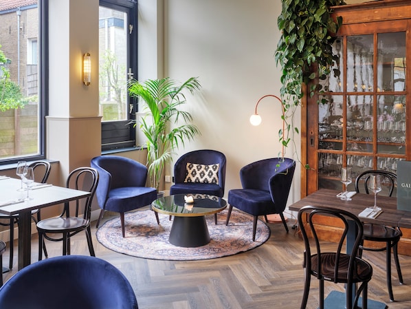 A cozy dining area with round tables, dark blue chairs, a central coffee table, and a large potted plant.