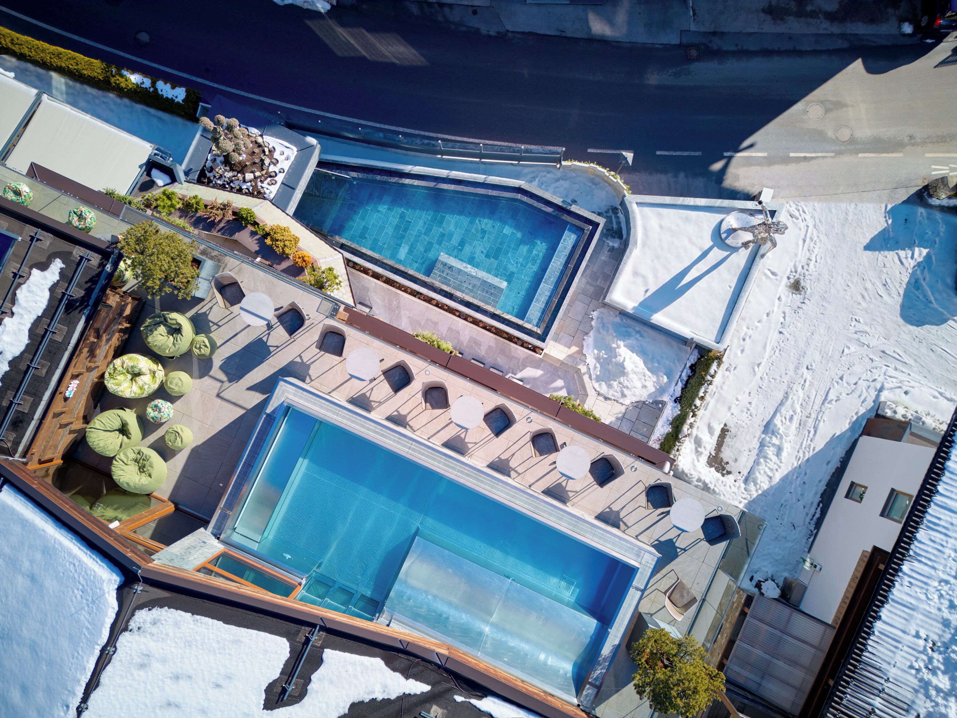 An aerial view of a resort with two swimming pools, outdoor seating, and snow on the ground.