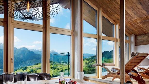 A dining area with a table set for two, large windows offering a mountain view, and a wooden ceiling. - Hotel Tirol (Fiss)