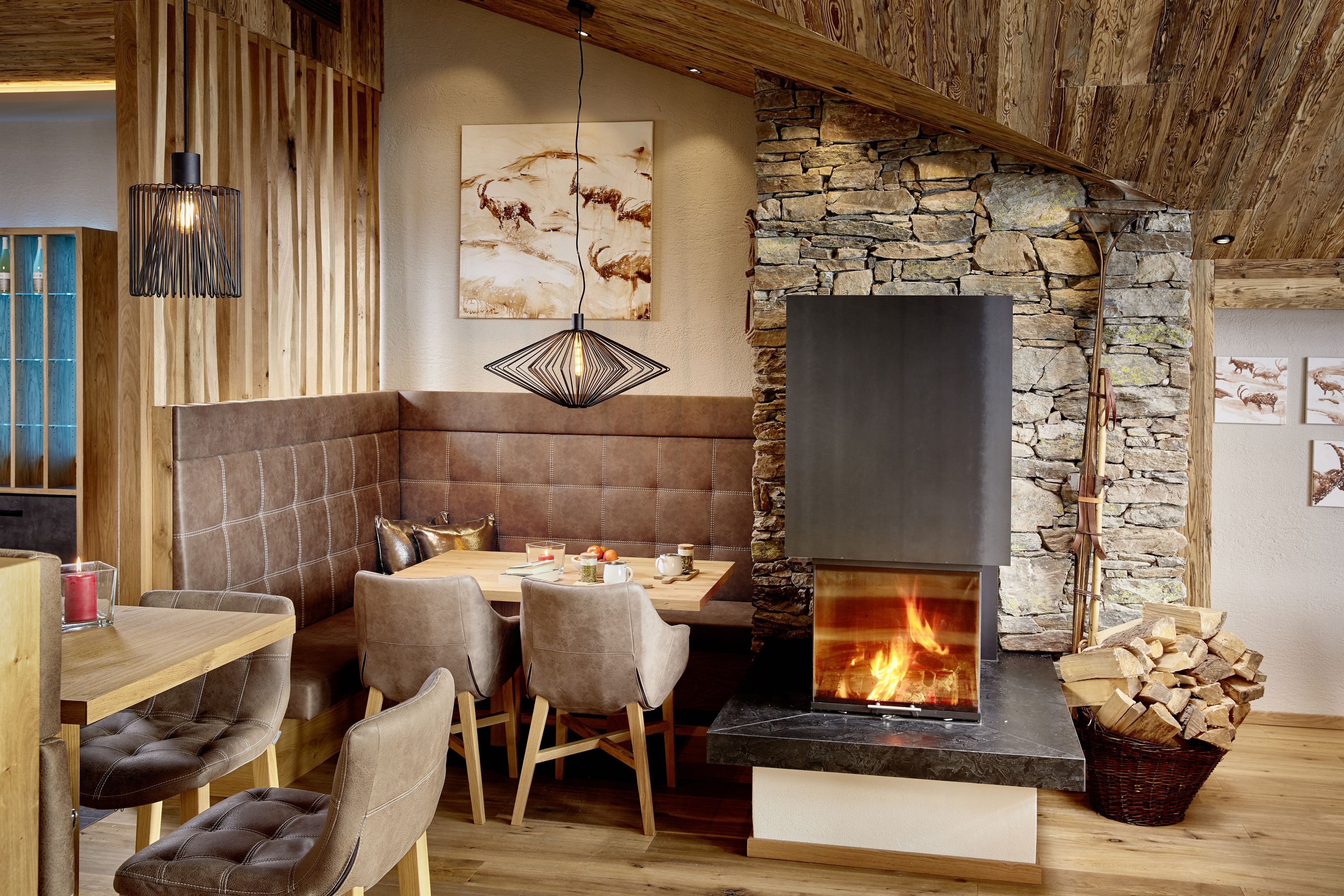 Un rincón comedor acogedor con chimenea de piedra, vigas de madera y una lámpara colgante moderna.