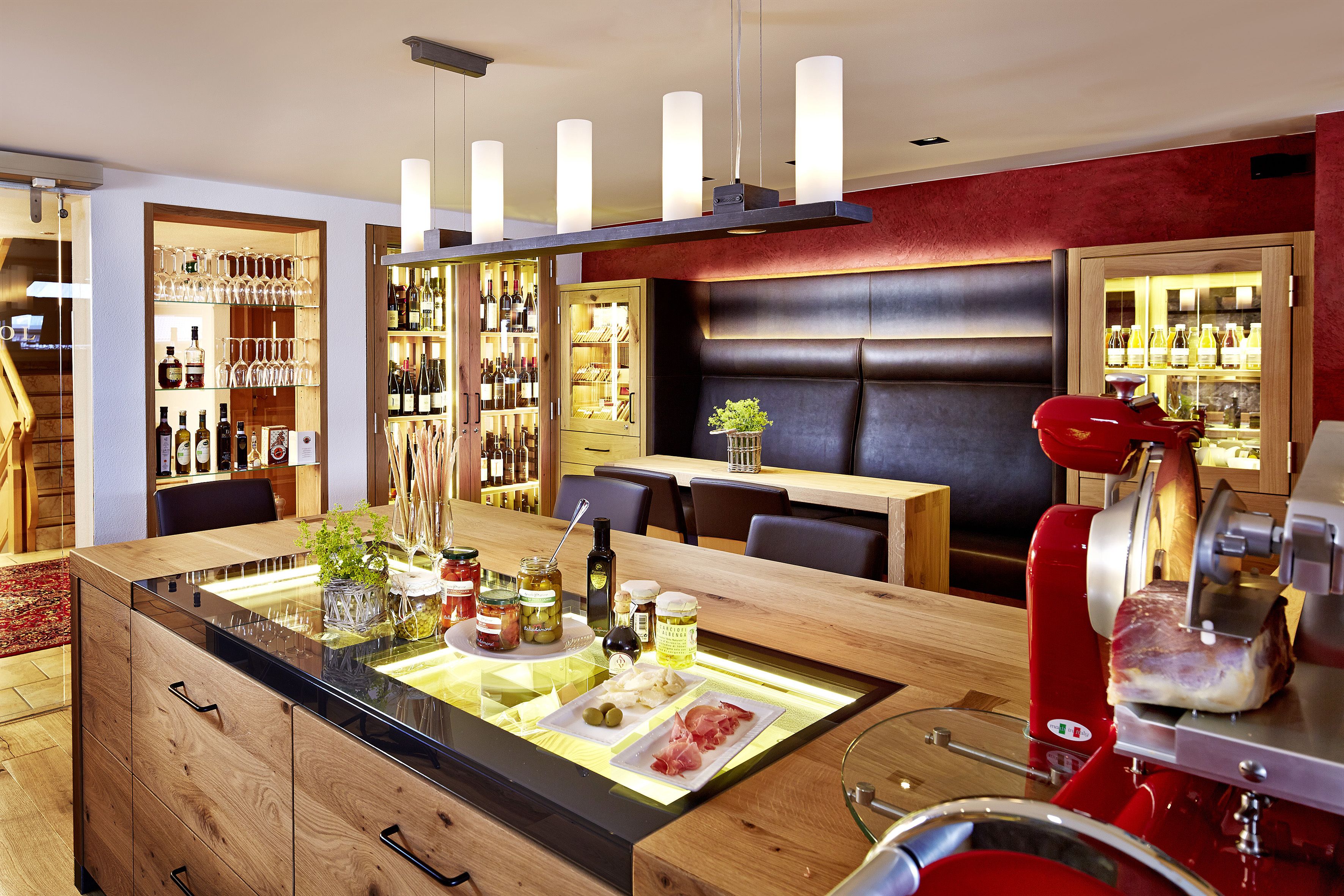 A modern kitchen with a central island, wooden cabinets, and a red meat slicer.