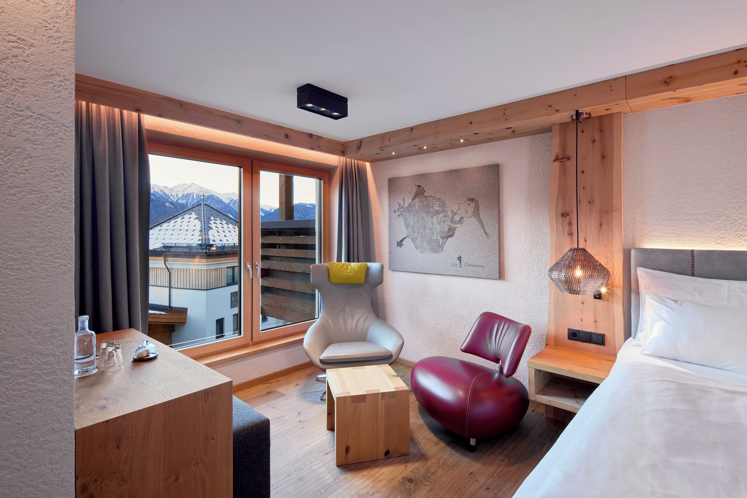 Ein modernes Hotelzimmer mit großem Fenster, einem Bett, einem Schreibtisch, einem Sessel und einem kleinen Tisch.