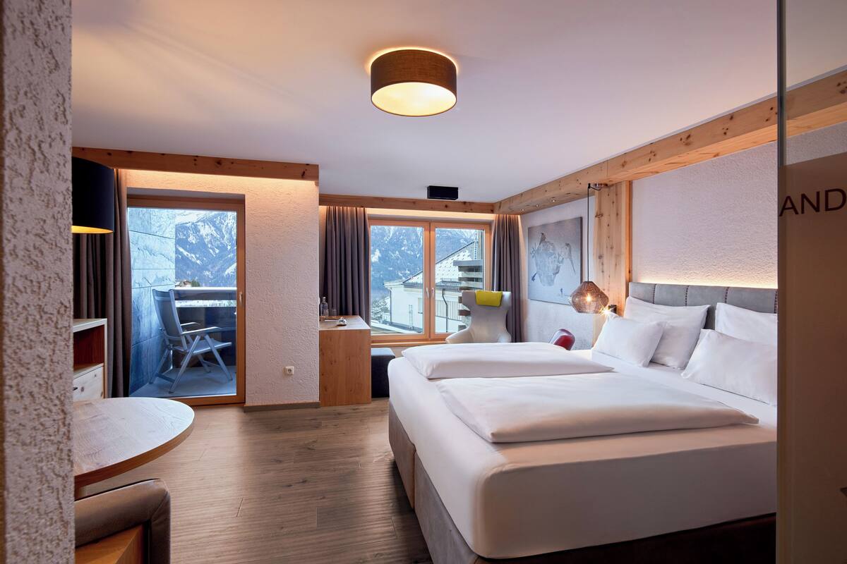A hotel room with a bed, a desk, a chair, a small table, and a window with a view.