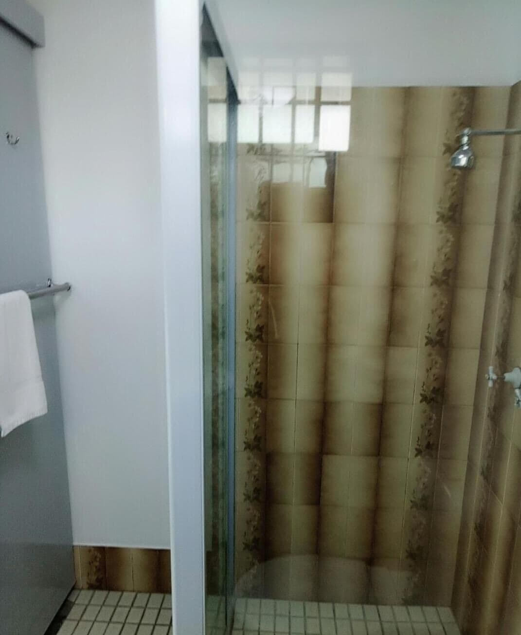 A bathroom with a glass shower enclosure, a white towel hanging on a rack, and a tiled floor.