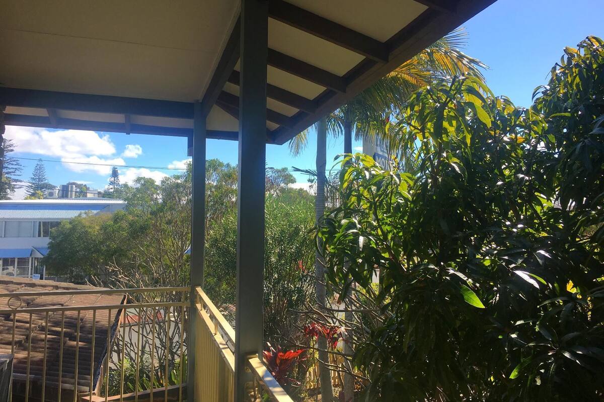 A covered balcony with a view of surrounding buildings and trees.