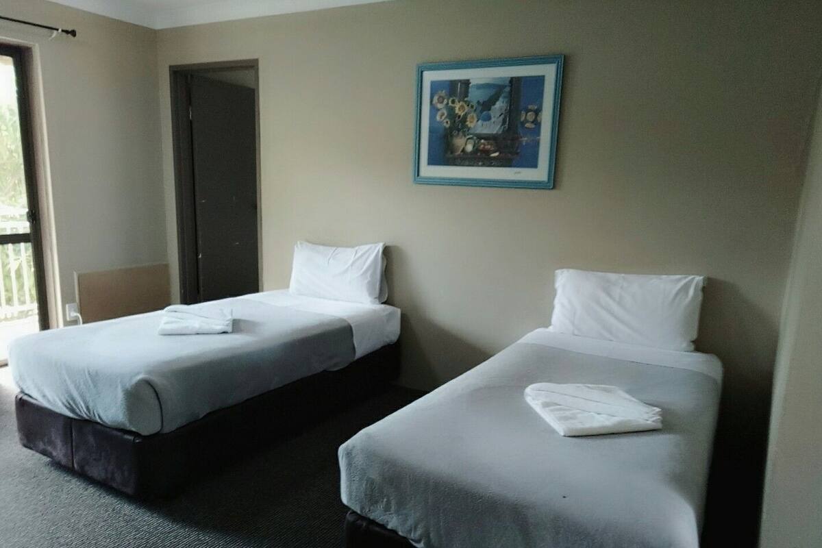 A hotel room with two single beds, a door, and a framed picture on the wall.