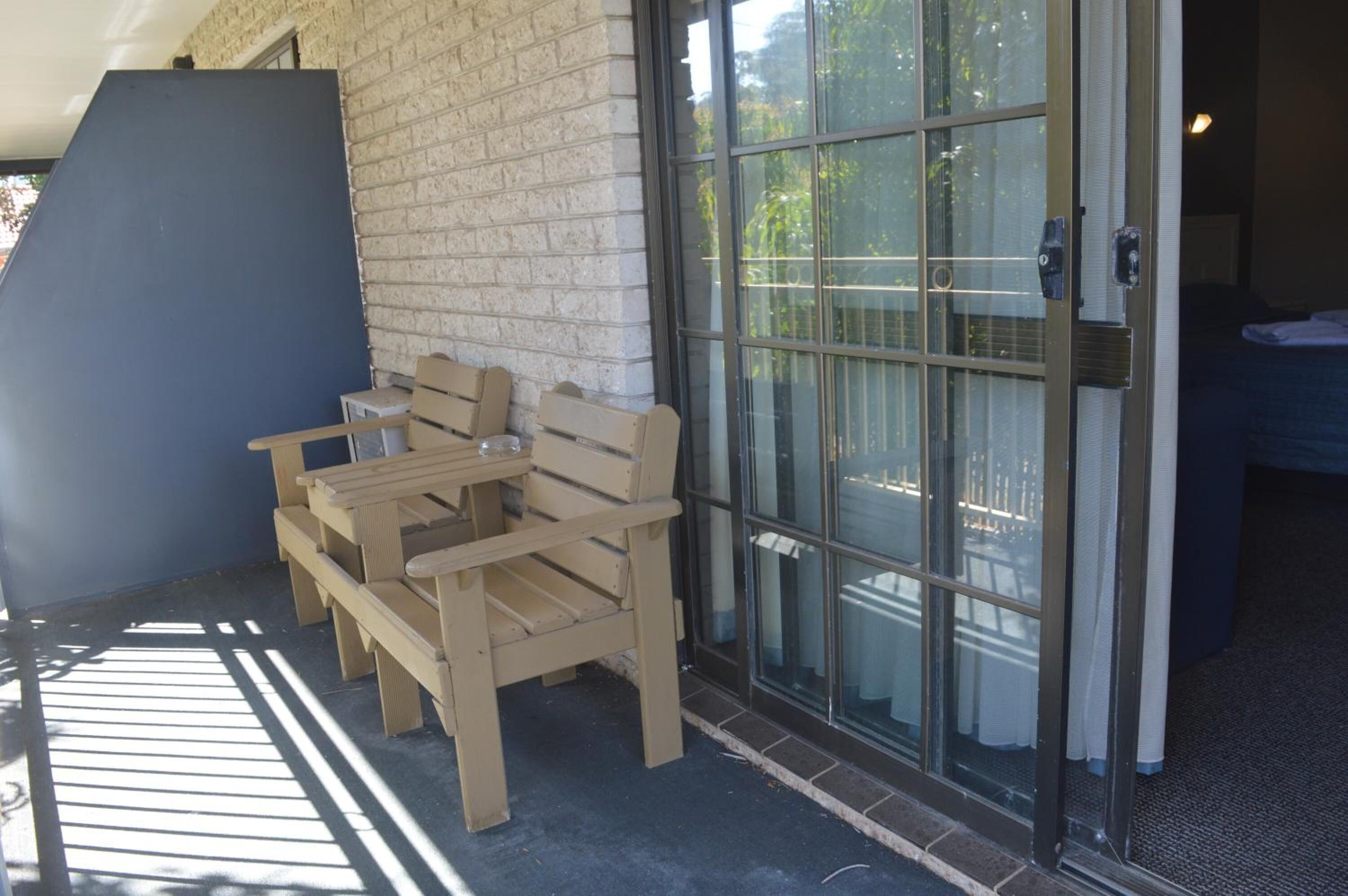 Un banco de madera frente a un edificio con puerta de vidrio y pared de ladrillo.