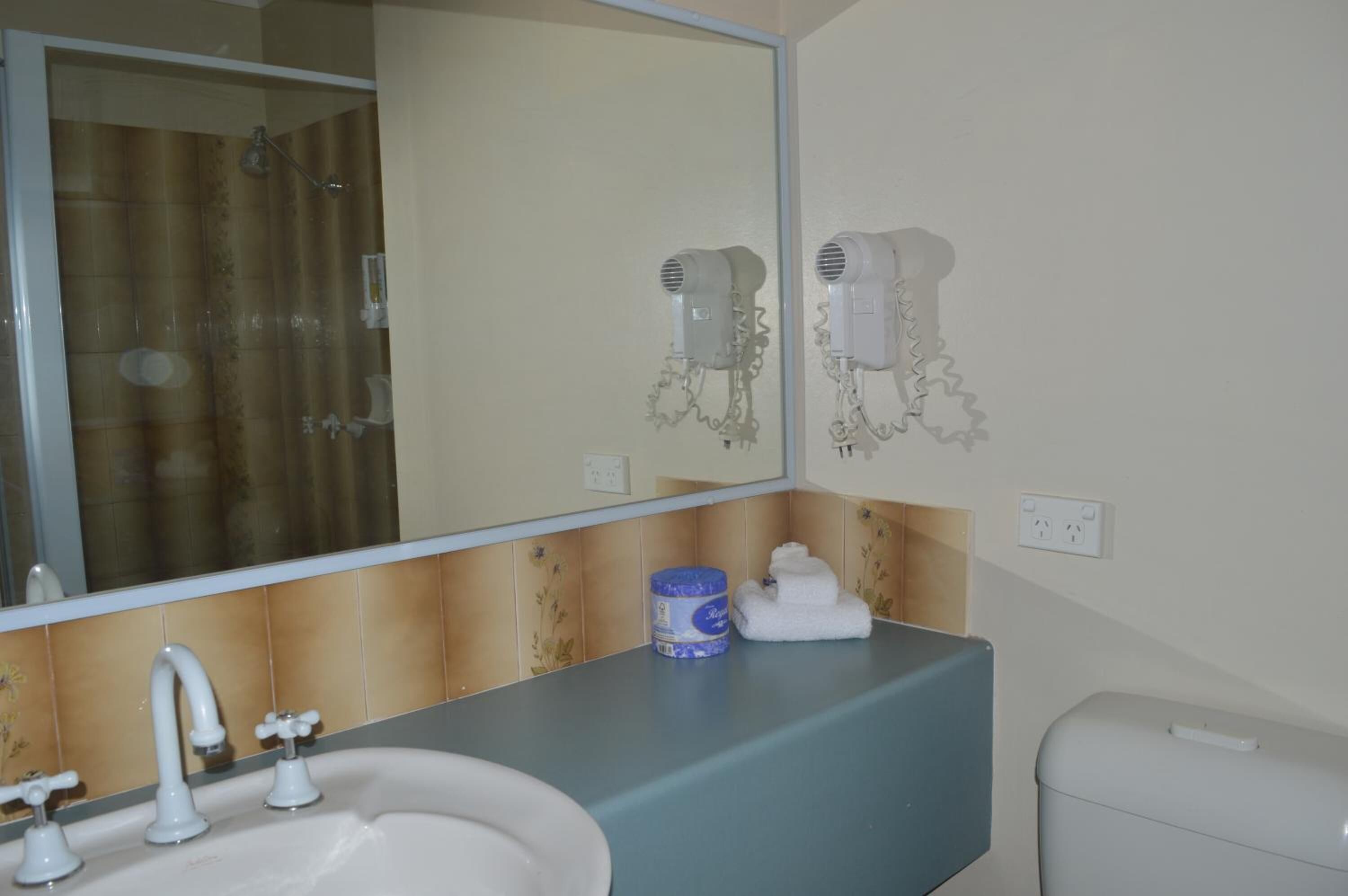 Un baño con lavamanos, espejo y dos secadores de pelo fijados a la pared.