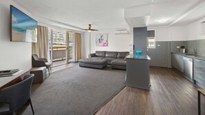 A modern living room with a sectional sofa, a dining area, and a kitchen with grey tiles. - El Motor Inn (Port Macquarie)