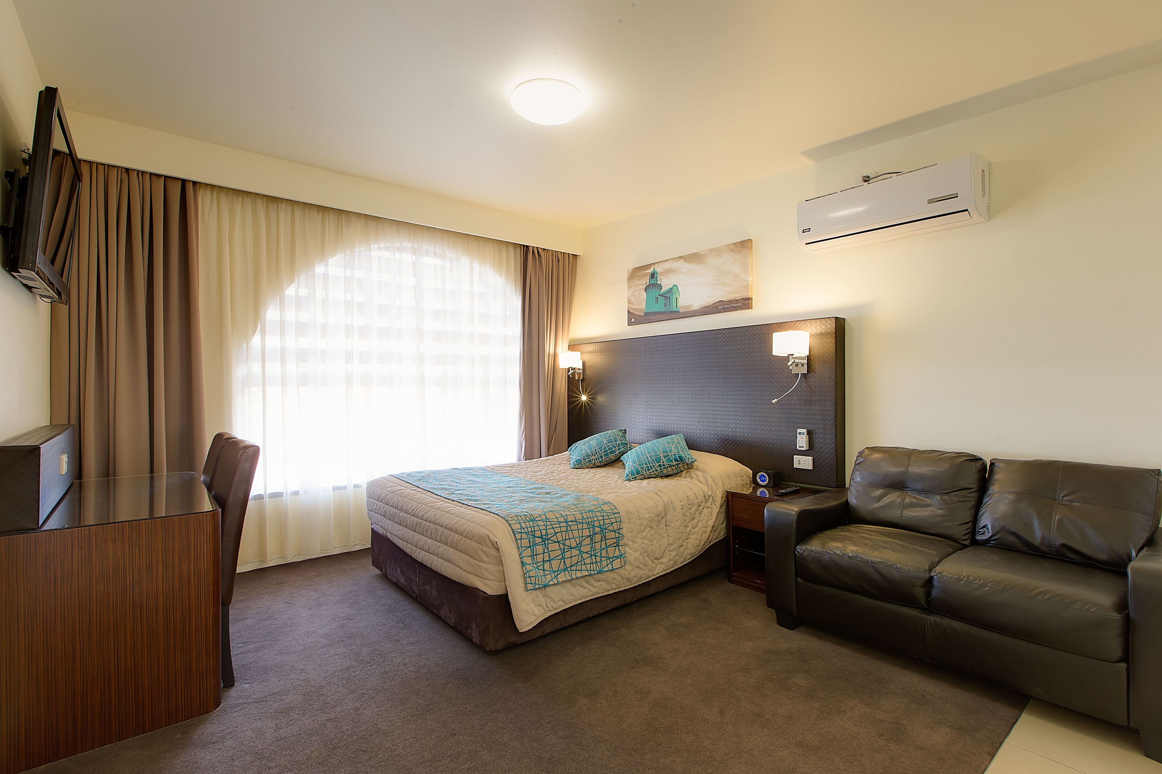 Habitación de hotel con cama, escritorio, sofá, televisión, aire acondicionado y un cuadro en la pared.