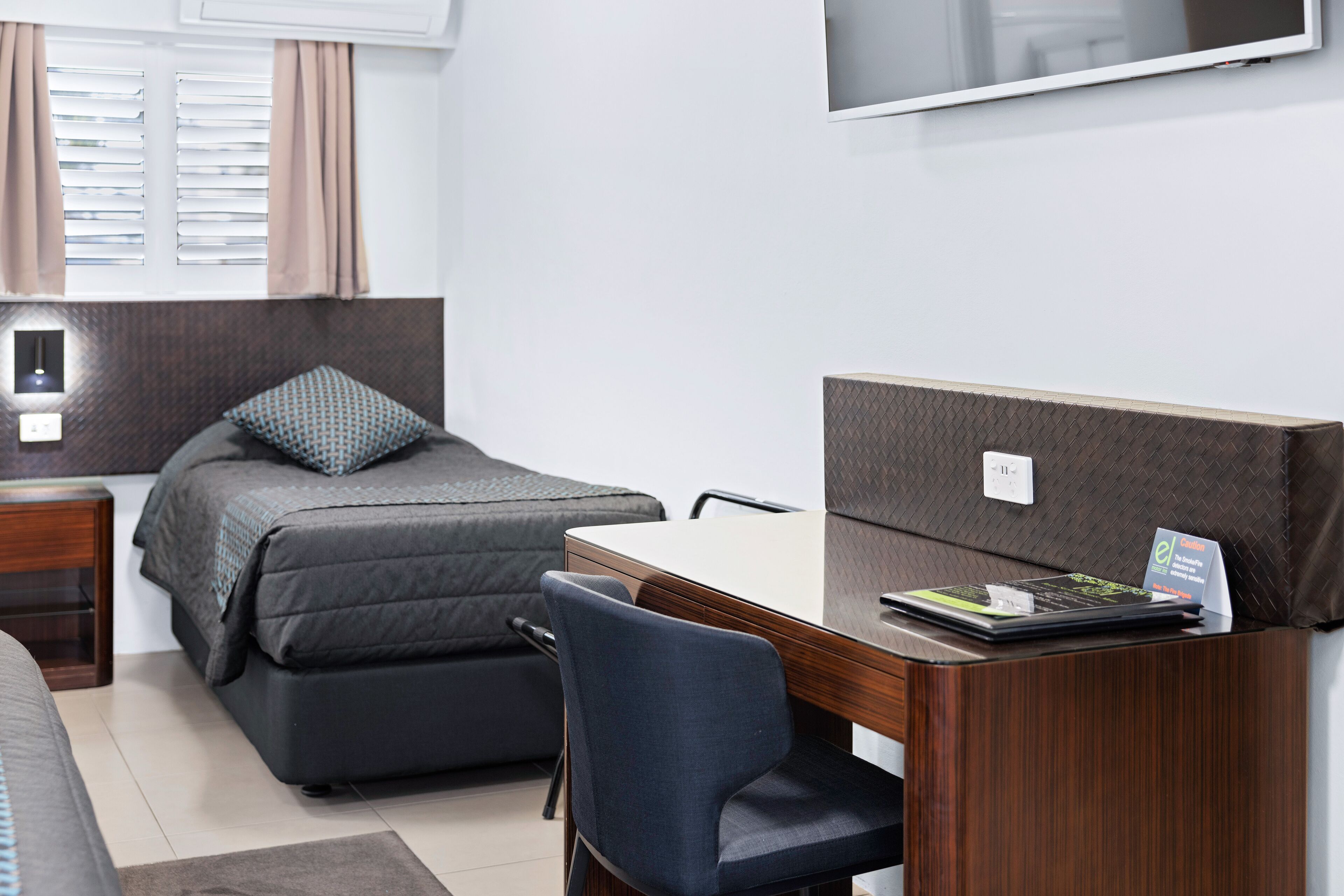 A bedroom with a bed, a desk, a chair, a TV, and a nightstand.