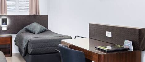 A bedroom with a bed, a desk, a chair, a TV, and a nightstand.