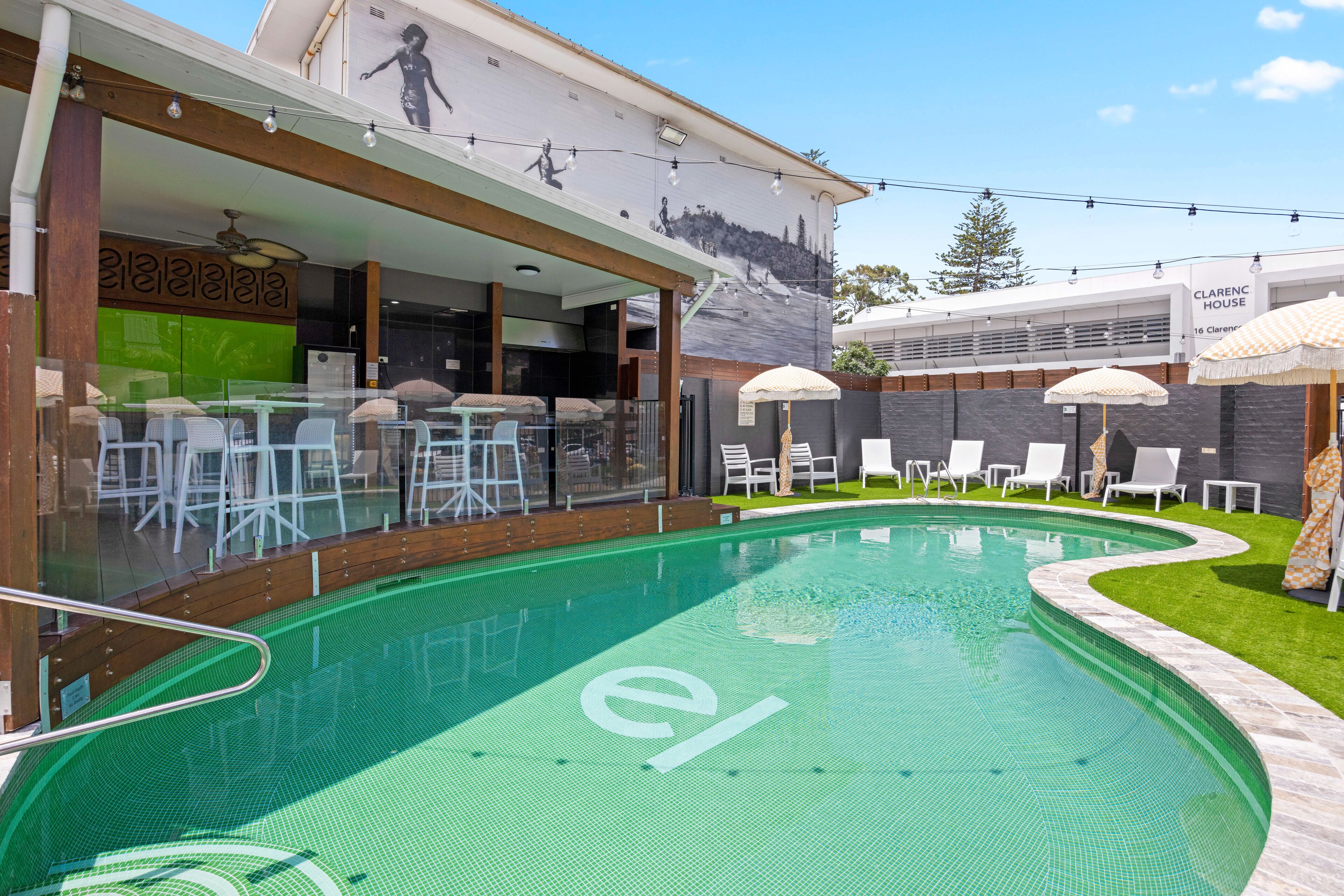 A swimming pool with a 'el' logo, outdoor seating, and a mural on the building.
