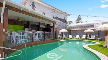 A swimming pool with a 'el' logo, outdoor seating, and a mural on the building.