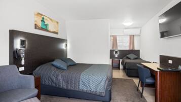 A modern hotel room with a large bed, a desk, a chair, and a sofa.