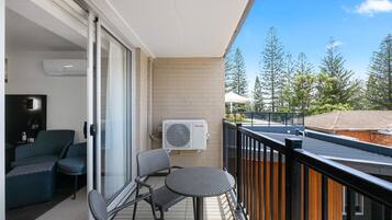 Een balkon met een schuifdeur, een tafeltje, twee stoelen en een airconditioner.