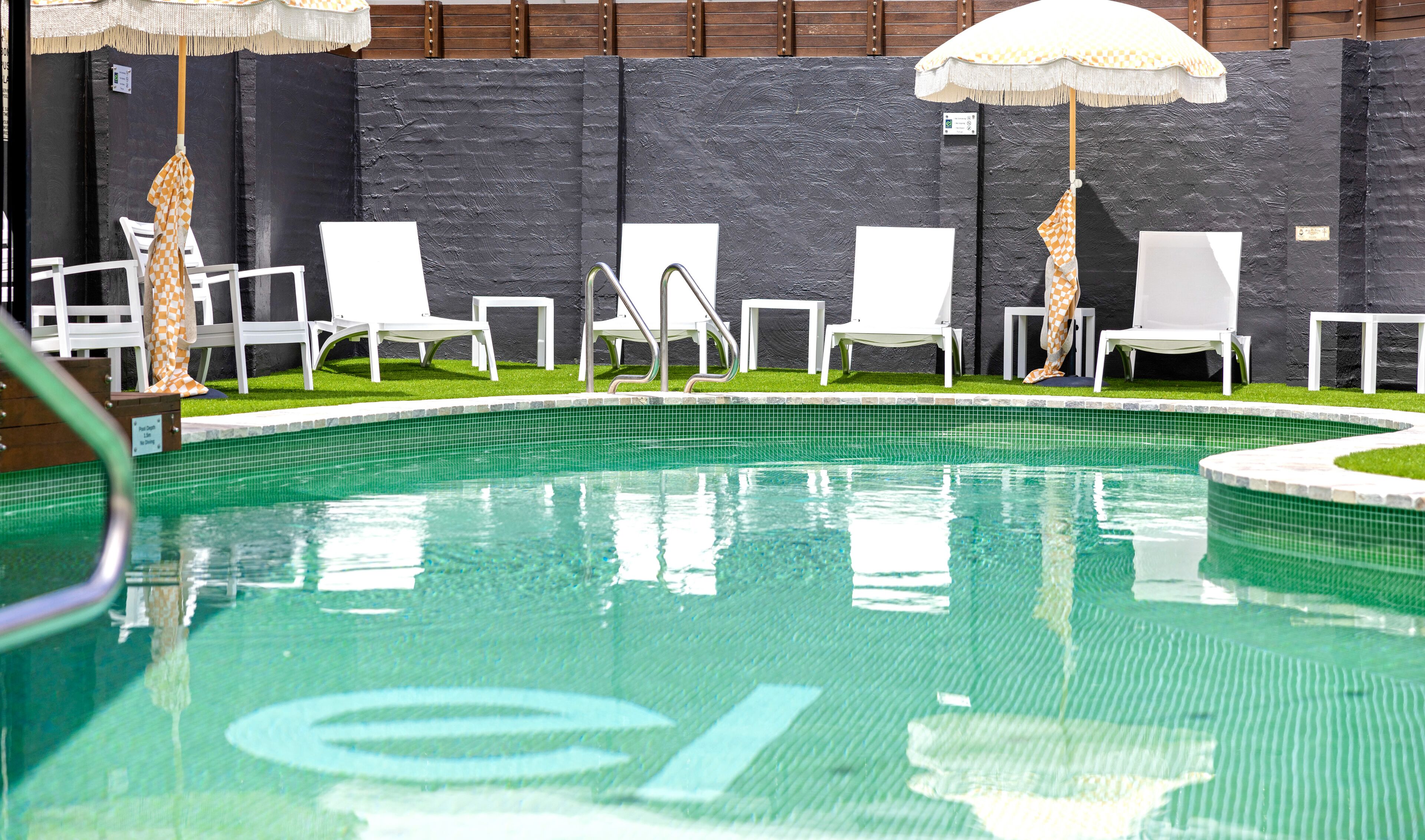 A swimming pool with white lounge chairs and umbrellas, surrounded by a stone wall.