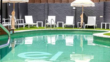 A swimming pool with white lounge chairs and umbrellas, surrounded by a stone wall.