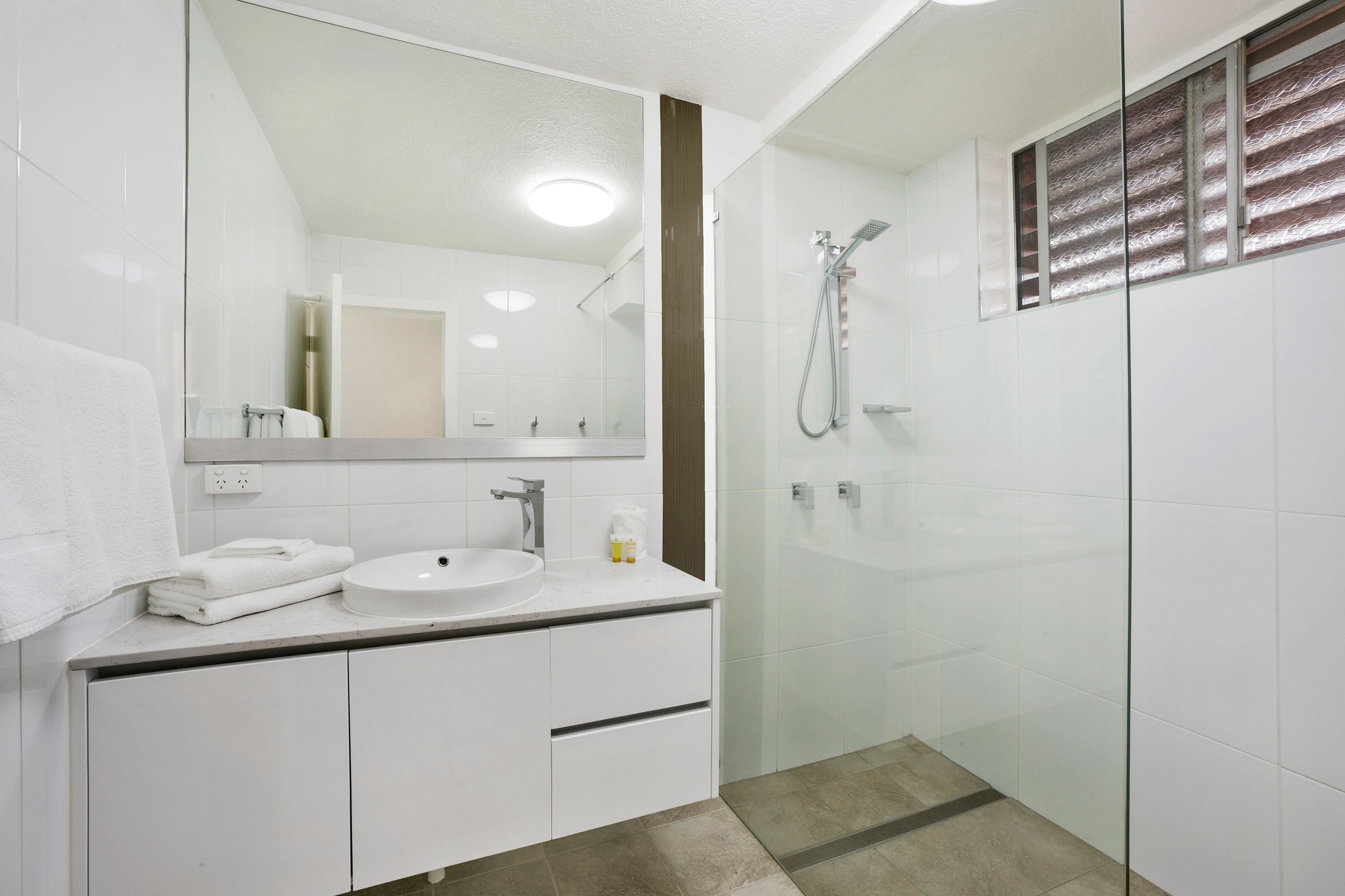 A modern bathroom with a glass-enclosed shower, a white sink, and a large mirror.