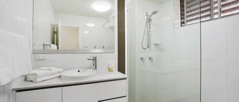 A modern bathroom with a glass-enclosed shower, a white sink, and a large mirror.