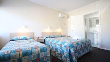 A hotel room with two beds, a bedside table, a nightstand, a mirror, and a bathroom with a sink and mirror.