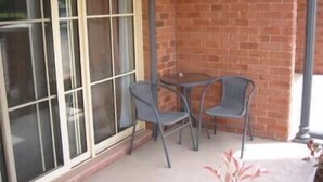A patio area with a brick wall, a glass door, and two metal chairs. - Gabriel Motor Inn (Gundagai)