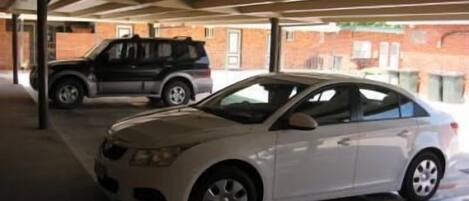 Un estacionamiento techado con un sedán blanco y un SUV negro aparcados.