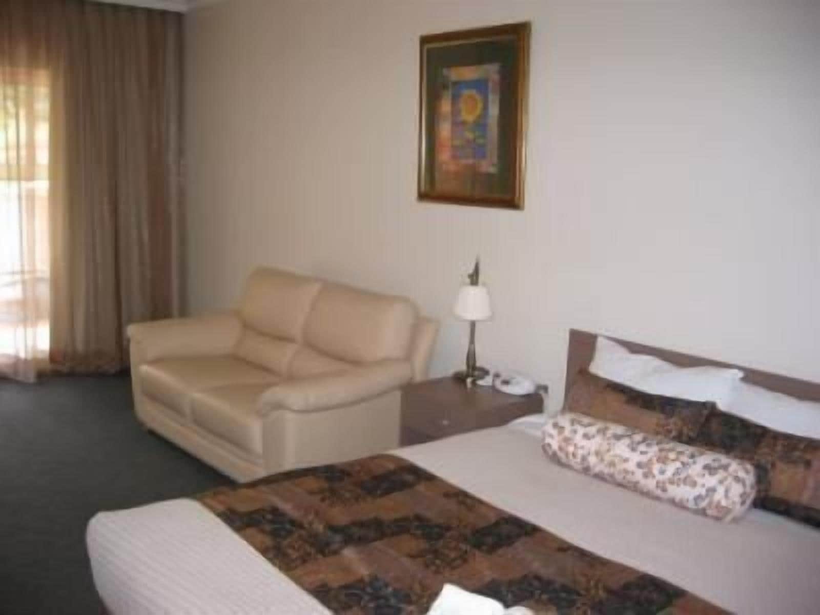 A hotel room with a bed, a sofa, a nightstand with a lamp, and a painting on the wall.