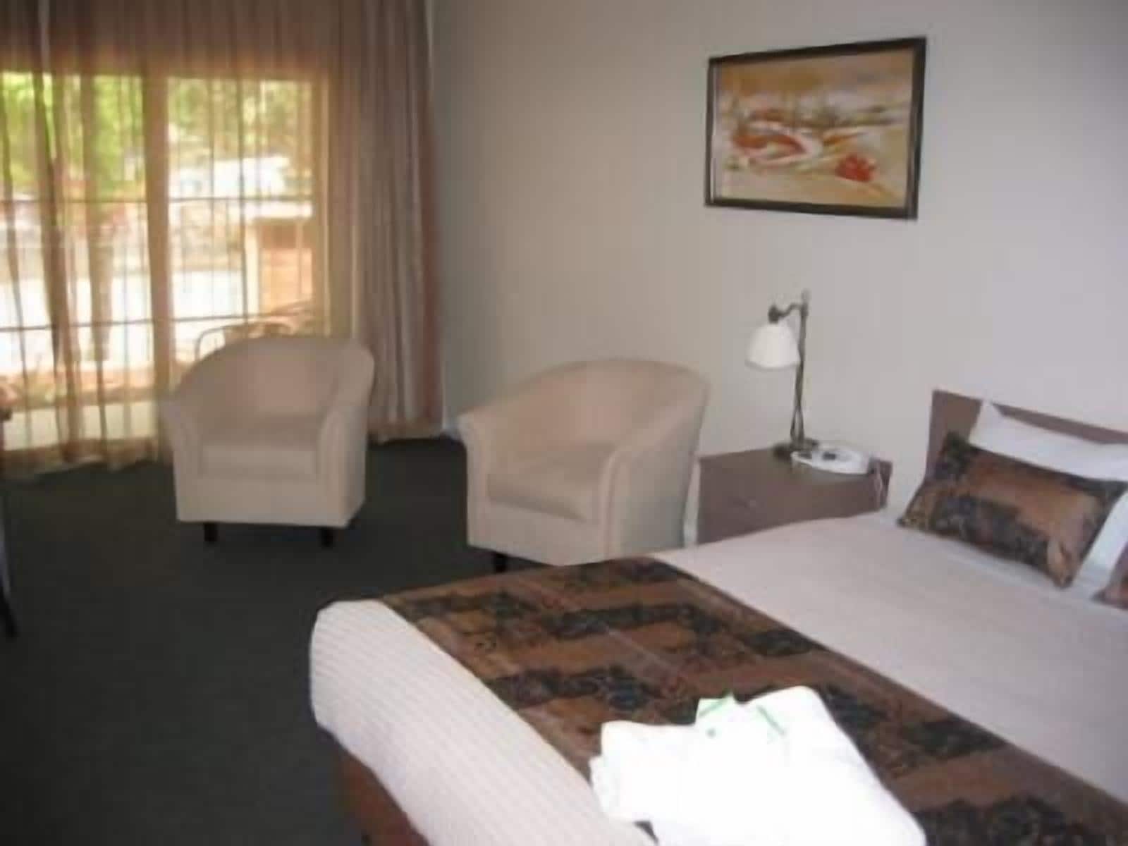 A hotel room with a bed, two armchairs, a nightstand, and a painting on the wall.