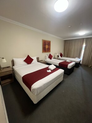 A hotel room with two beds, each with white linens and red pillows, a red throw blanket, a painting on the wall, and a large window with curtains. - Gabriel Motor Inn (Gundagai)