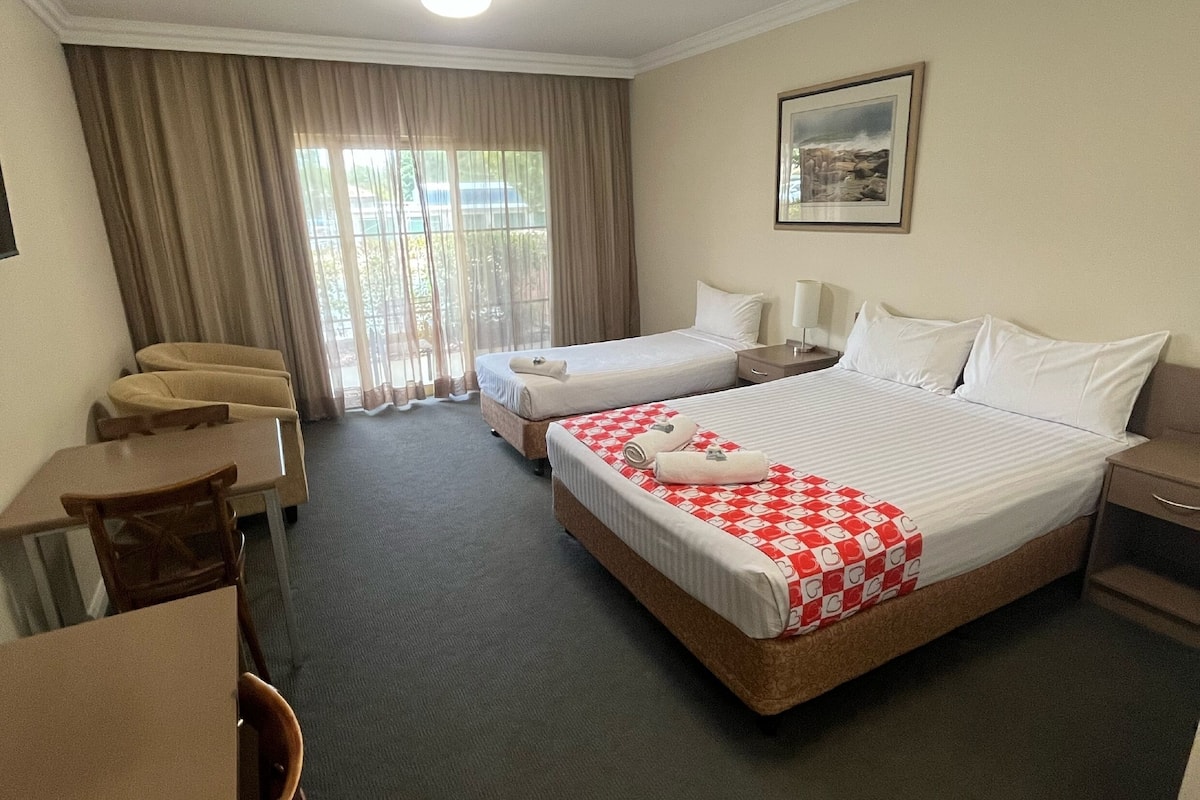 A hotel room with two beds, a desk, a chair, a lamp, and a window with curtains.