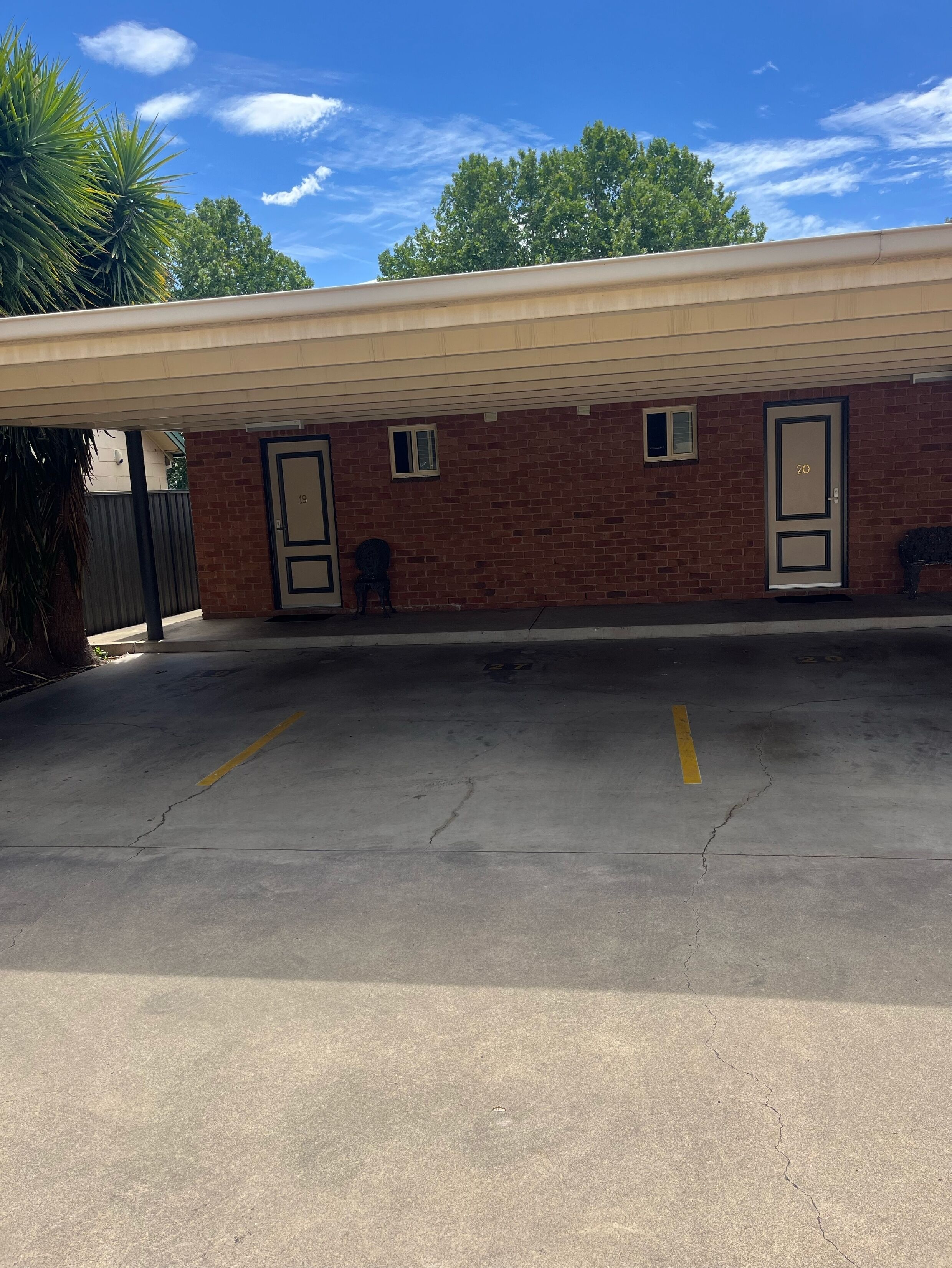 A parking area with a brick building, numbered doors, and a covered walkway.