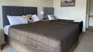 A double bed with a dark brown quilted bedspread and a grey upholstered headboard. There are two bedside tables with lamps and a small painting on the wall. - Citrus Motel (Griffith)
