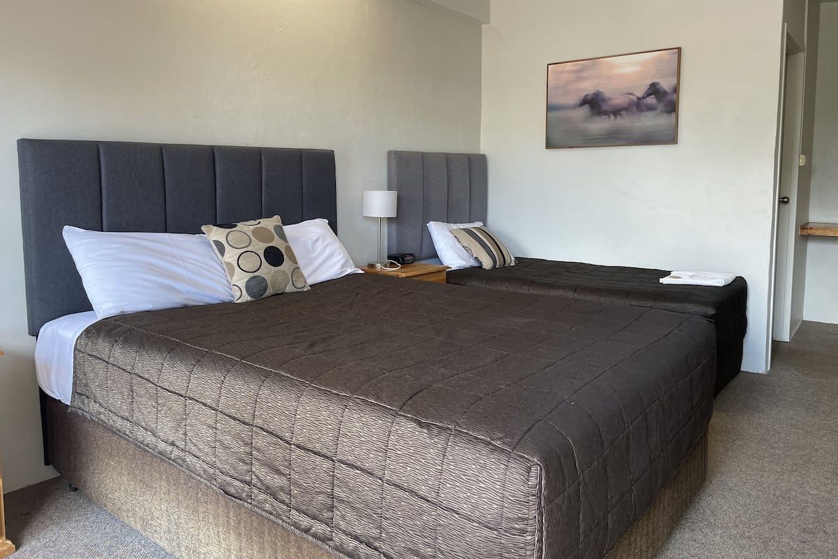 Una cama doble con colcha acolchada marrón oscuro y cabecera tapizada en gris. Hay dos mesitas de noche con lámparas y un pequeño cuadro en la pared.