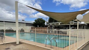 A swimming pool with a white fence, a shaded area, and a view of buildings in the background. - Citrus Motel (Griffith)