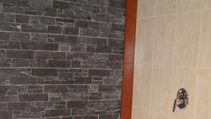 Une salle de bain avec un mur en pierre, une baignoire et un espace douche.