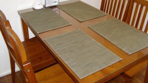 Une table de salle à manger en bois, avec quatre sets de table carrés et un présentoir à menus.